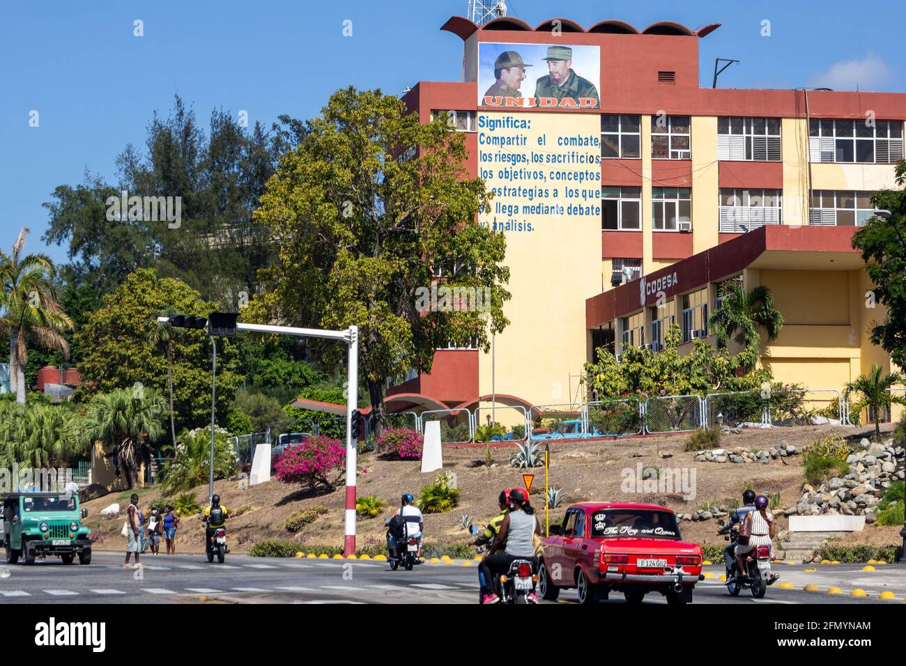 Verkehr und Lifestyle in der Avenida Garzon. Gebäude von CODESA mit den Bildern von Fidel Castro und Raul Castro, Santiago de Cuba, Kuba Stockfoto
