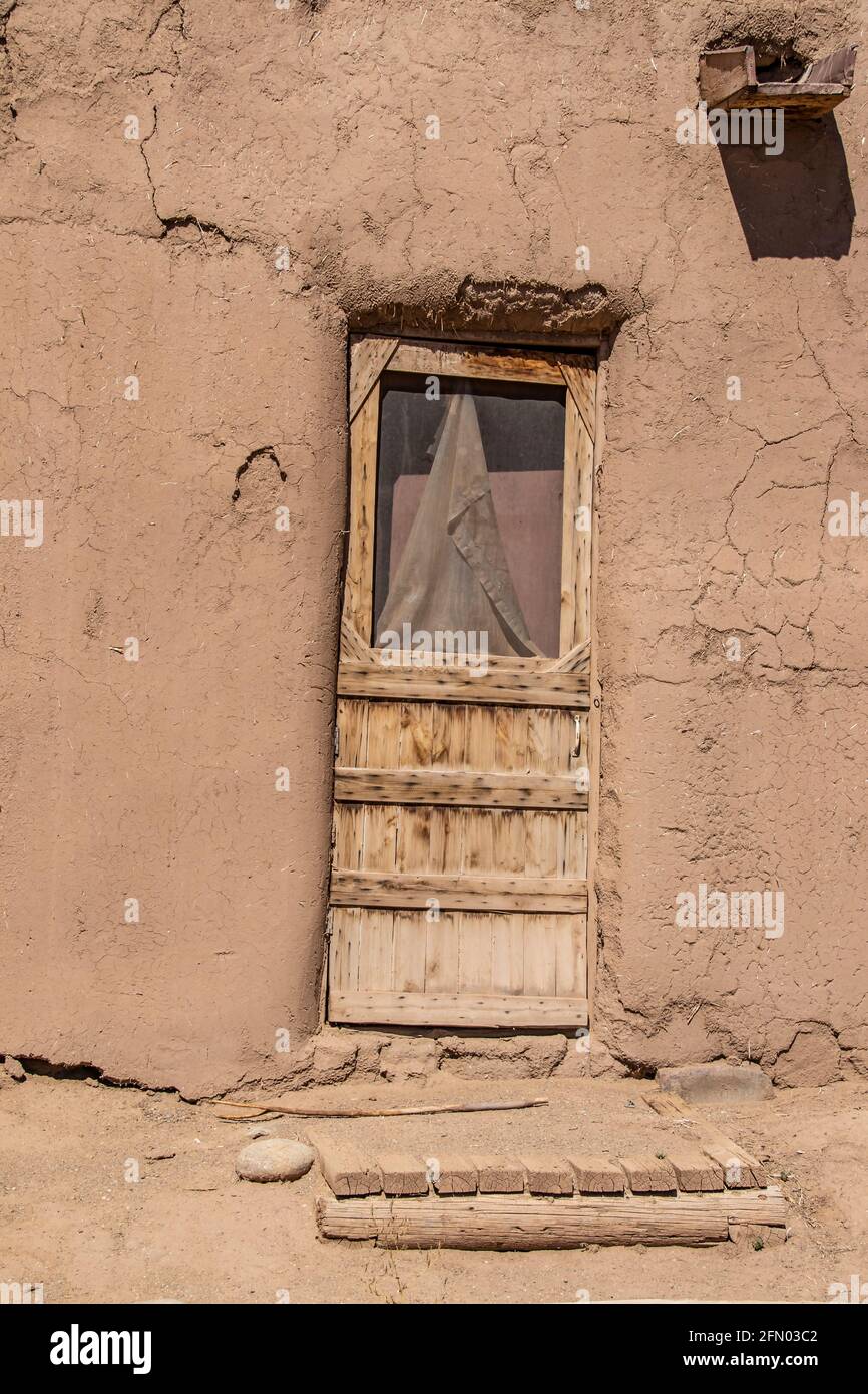 Rauh gehauene Holztür mit beschädigtem Schirm und hölzerner Veranda Im lehmziegelpueblo, das in Taos New Mexico wohnt Stockfoto