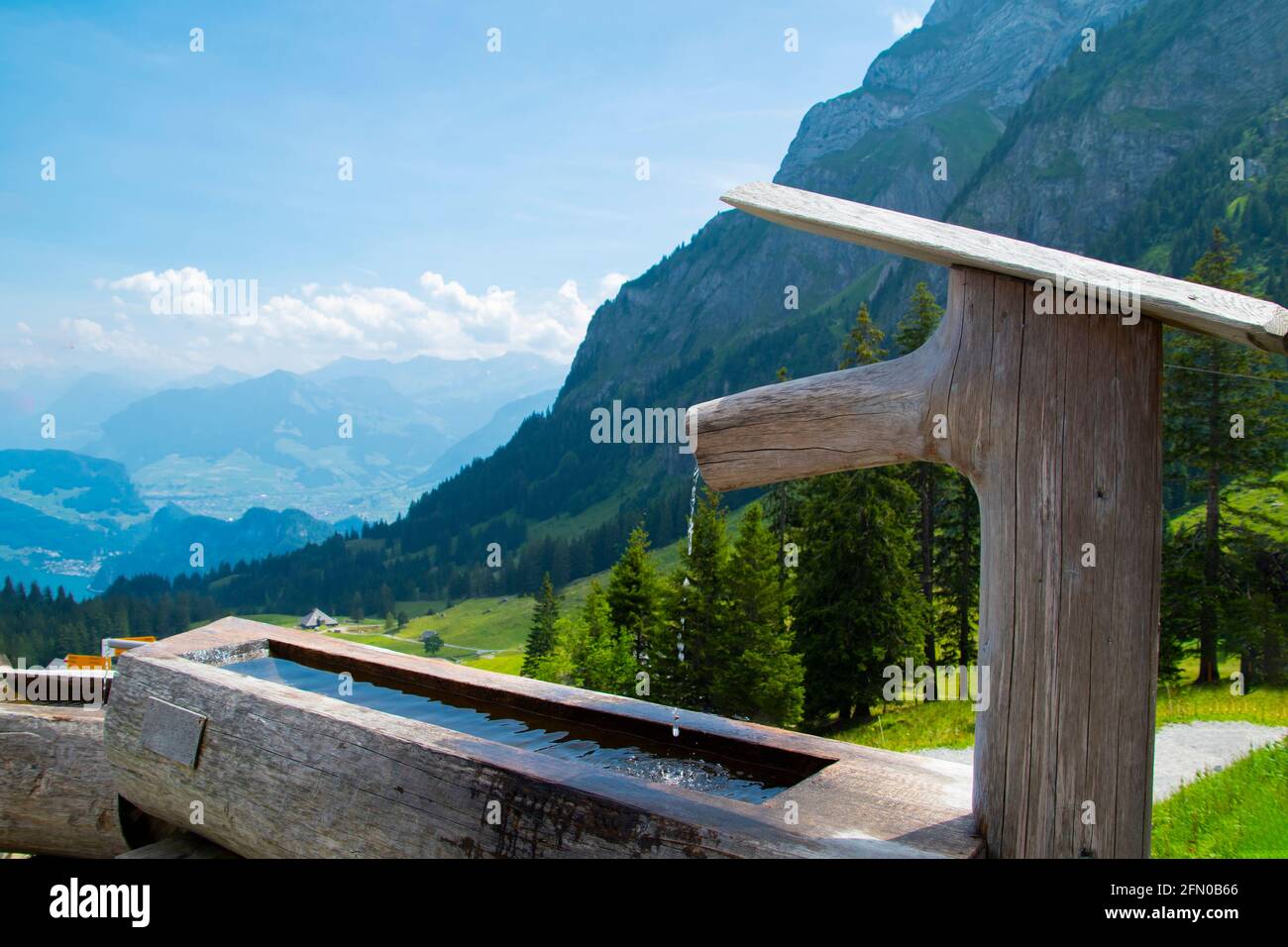Holzbrunnen in den alpen mit Blick auf die alpen Bergbäume grüne Hügel und blauer Himmel Stockfoto