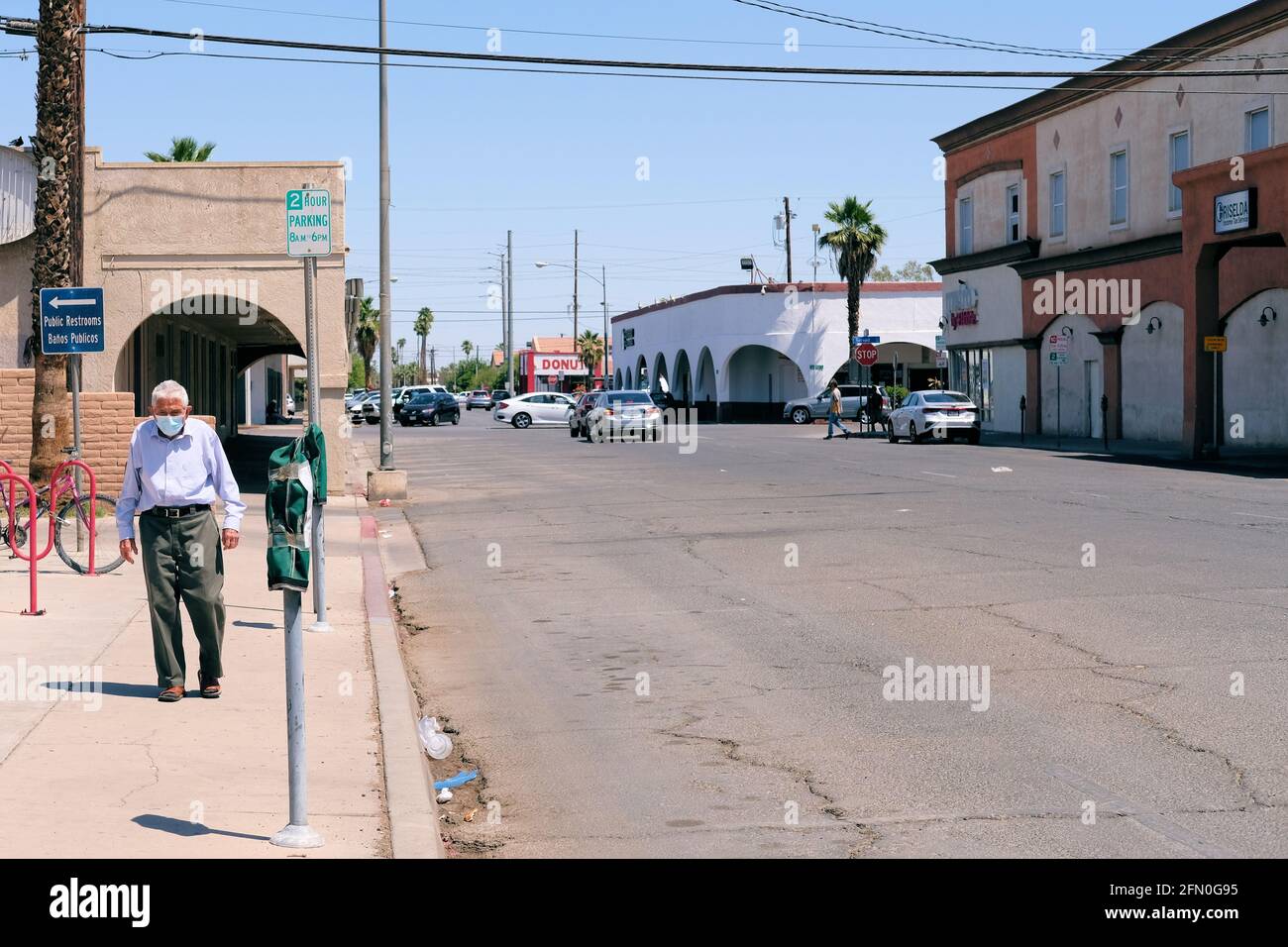 Maskierter alter Mann, der während der Pandemie von Covid-19 allein auf einem Bürgersteig in einem nahe leeren Stadtzentrum von Calexico, Kalifornien, ging; älterer Herr ganz allein. Stockfoto
