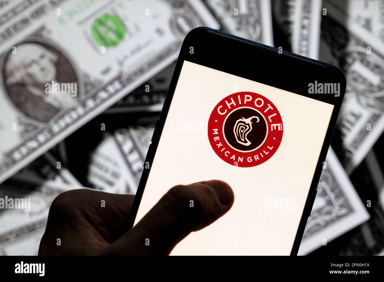 In dieser Abbildung ist das Logo der amerikanischen Fast-Food-Restaurantkette Chipotle Mexican Grill zu sehen, das auf einem Smartphone mit einer Währung in USD (US-Dollar) im Hintergrund angezeigt wird. Stockfoto