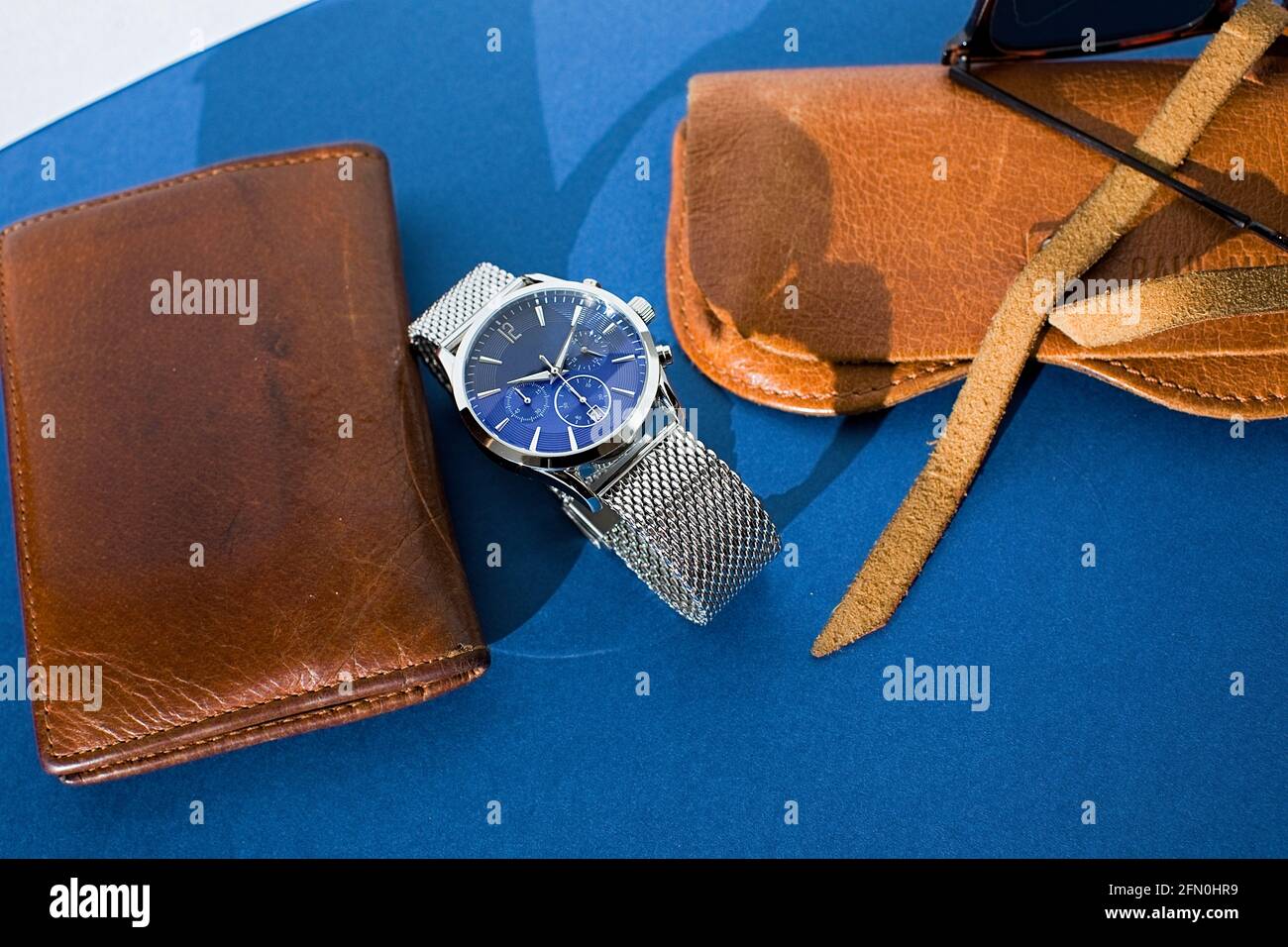 Ledertasche, Uhr mit Metallarmband, Sonnenbrille und Laptop auf blauem Hintergrund. Accessoires für Herren. Draufsicht Stockfoto