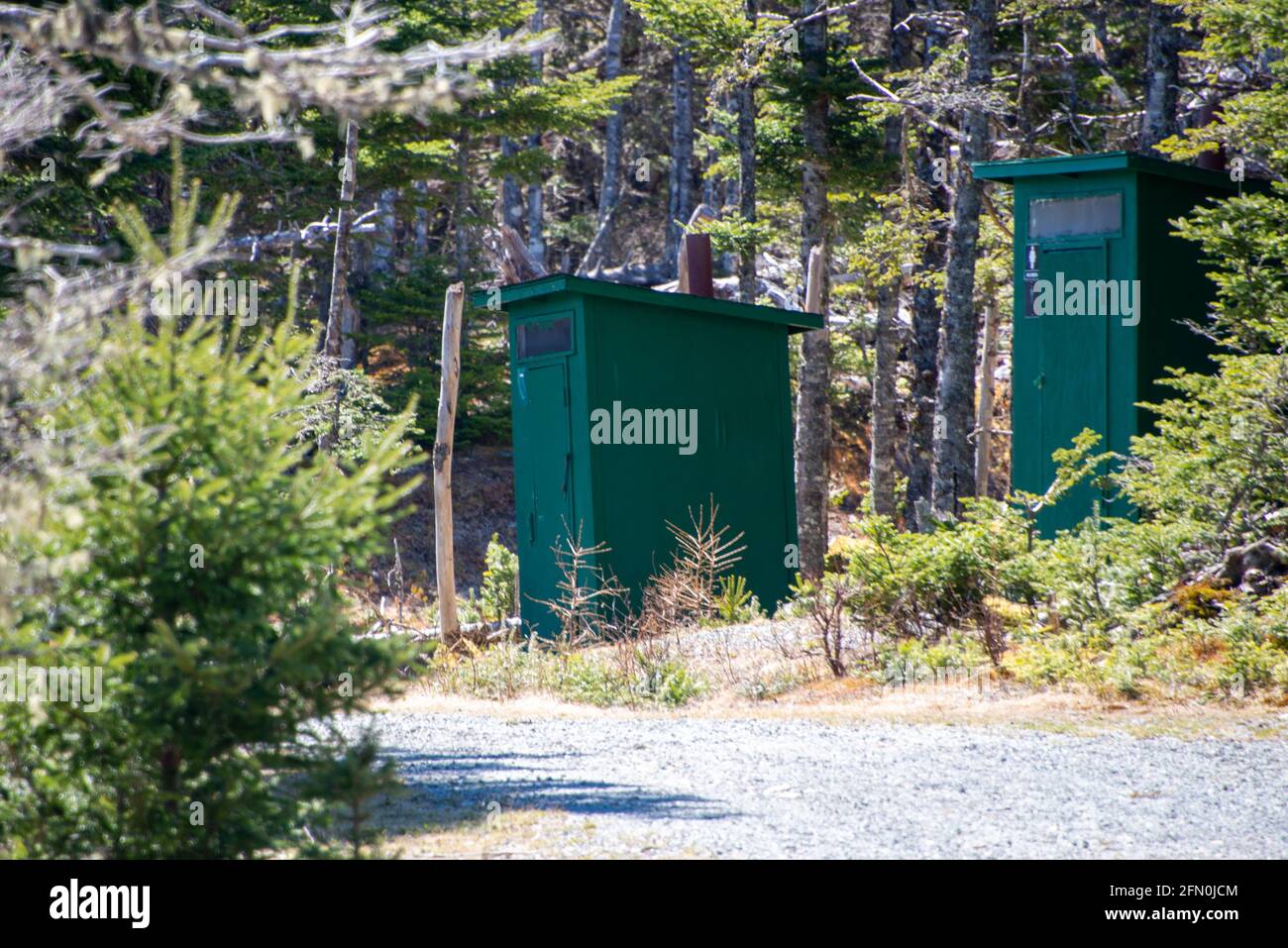 Zwei grüne hölzerne Nebengebäude oder Badezimmer sind in den Wäldern auf einem Campingplatz und Park versteckt. Es gibt eine Schotterstraße, die zu den privaten Gebäuden führt. Stockfoto
