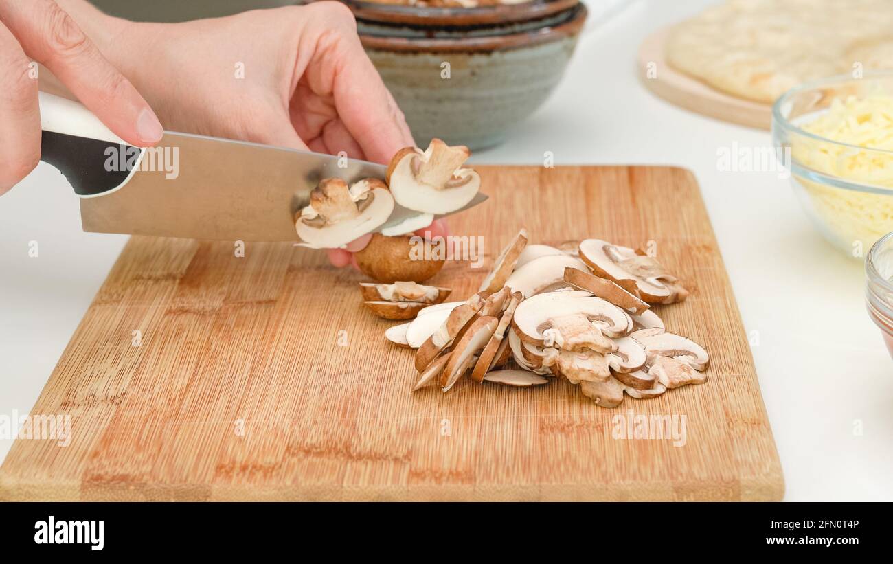 Frau schneidet Crimini Pilze auf Holz Schneidebrett. Schritt für Schritt Pilz Pizza Rezept Stockfoto