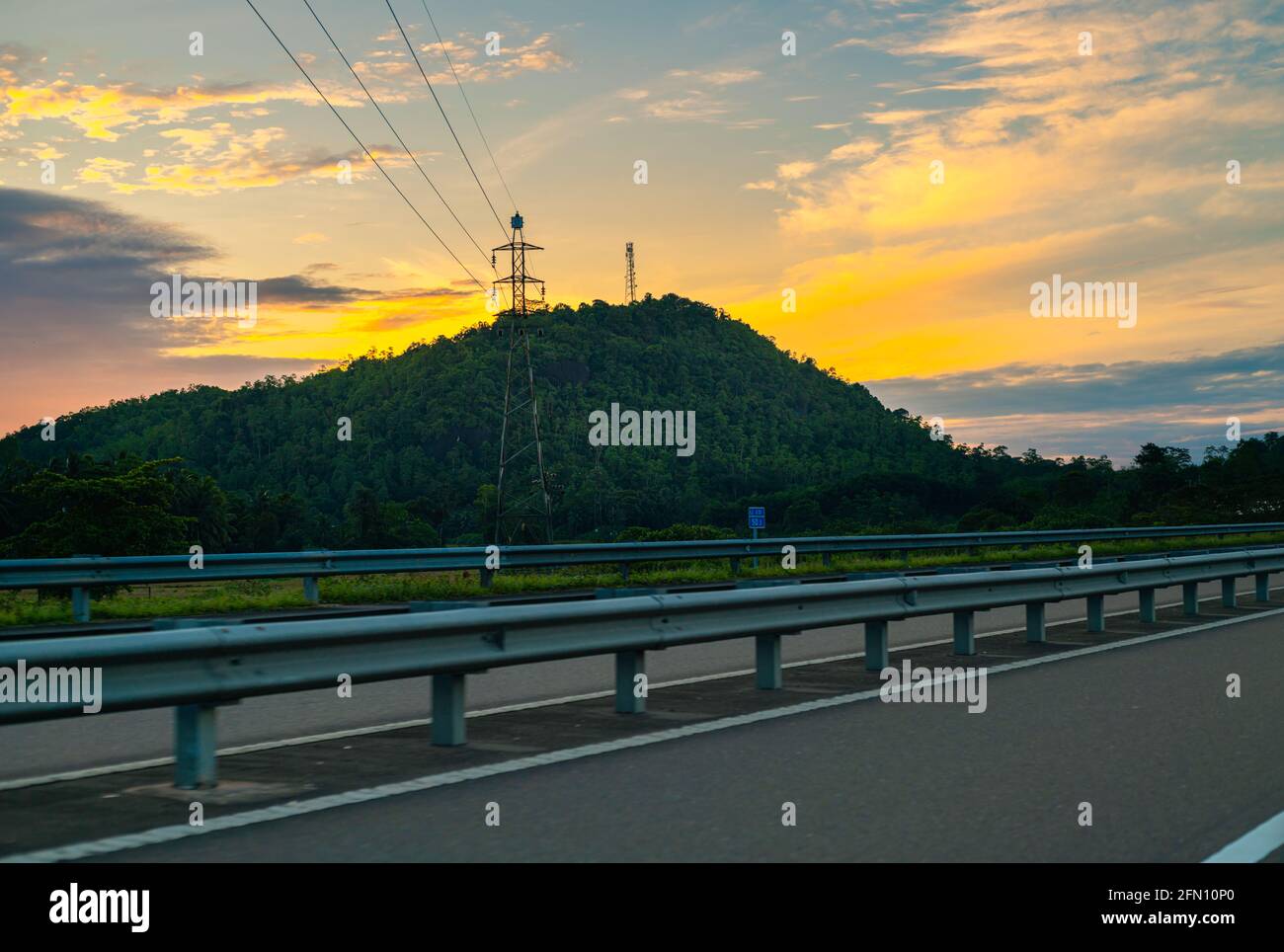 Expressway wunderschöne Landschaft am Straßenrand, aufgehende Sonne hinter den Bergen und führende Drähte zu den Bergspitzen-Pylonen. Stockfoto