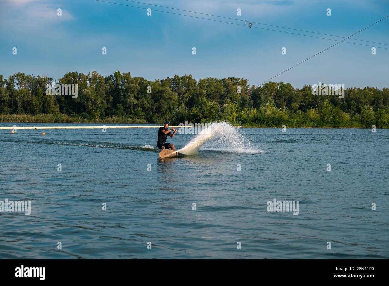Sportlicher Mann, der am Sommertag auf dem Wakeboard auf dem Fluss reitet Stockfoto