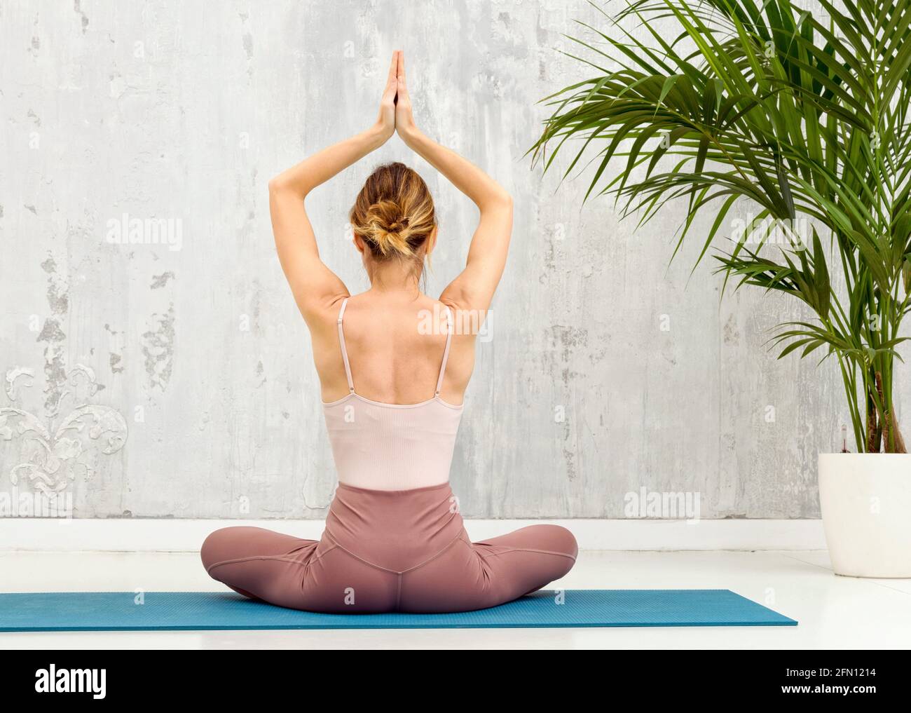 Rückansicht einer Frau in der Sukhasana Yoga-Pose Sitzend in der Lotusposition mit im Gebet erhobenen Händen Während der Meditation Stockfoto
