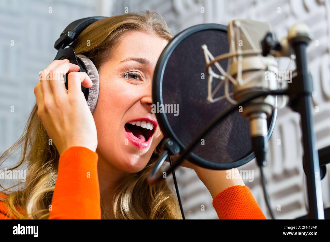 Junge weibliche Sänger oder Musiker mit Mikrofon- und Kopfhöreranschluss für Audio-Aufnahme im Studio Stockfoto