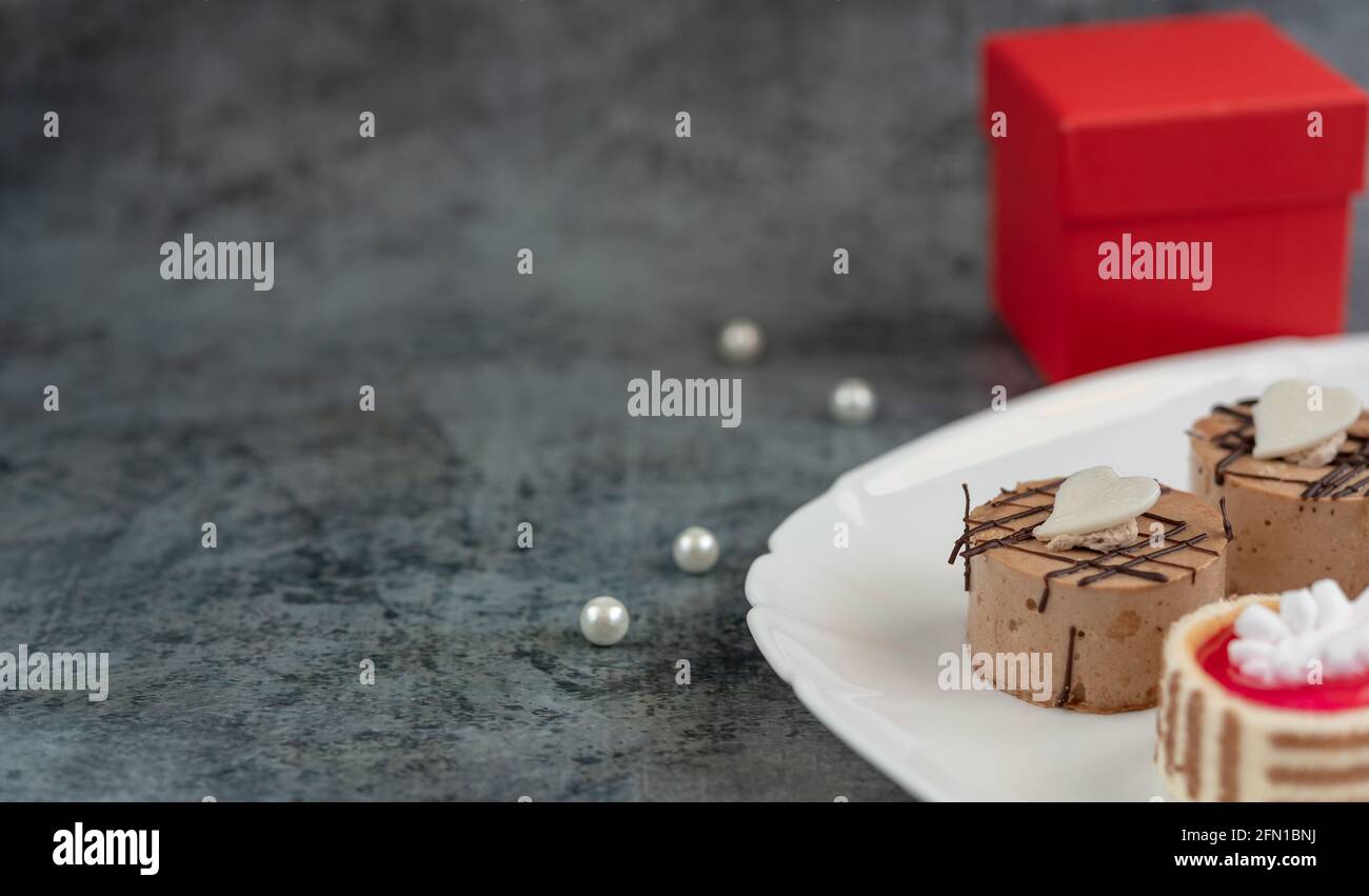 Festlicher Hintergrund mit roter Geschenkbox, weißen Perlen und Mini-Kuchen Stockfoto