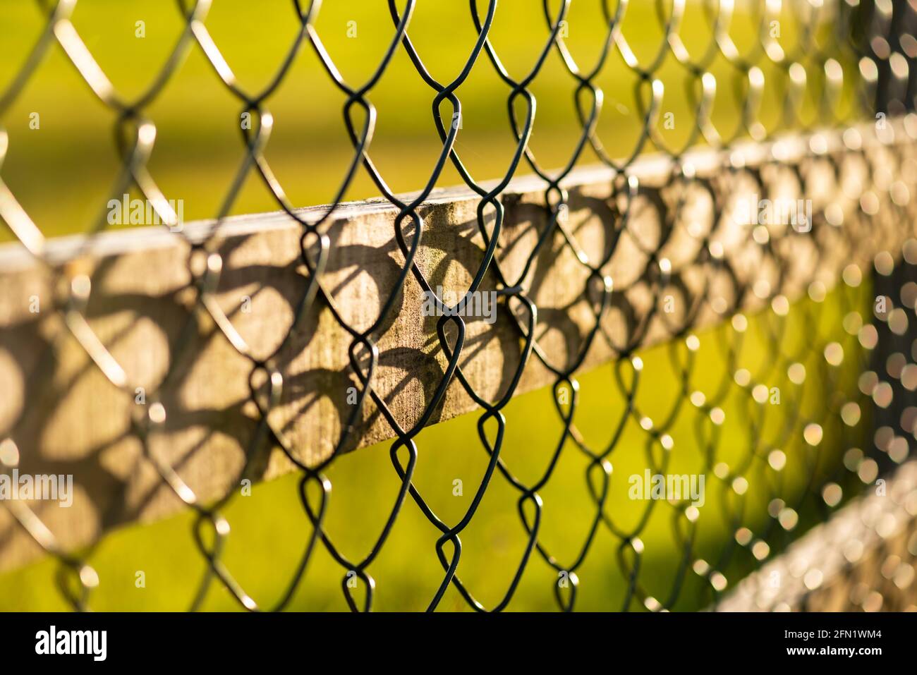Nahaufnahme des Diamantmusters des Drahtzeichenzauns mit extrem geringer Schärfentiefe entlang eines Gehwegs. Stockfoto