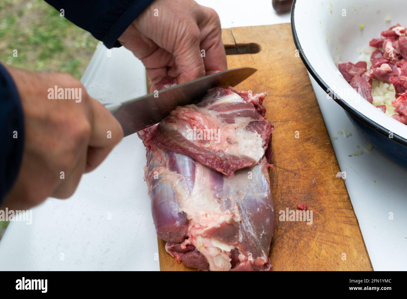 Frau schneidet rohes Fleisch auf kleine Stücke mit Küchenmesser Schneidebrett. Weibchen schneidet rotes Rinderfilet auf Holzbrett und hält das Messer in der Hand. Housewi Stockfoto