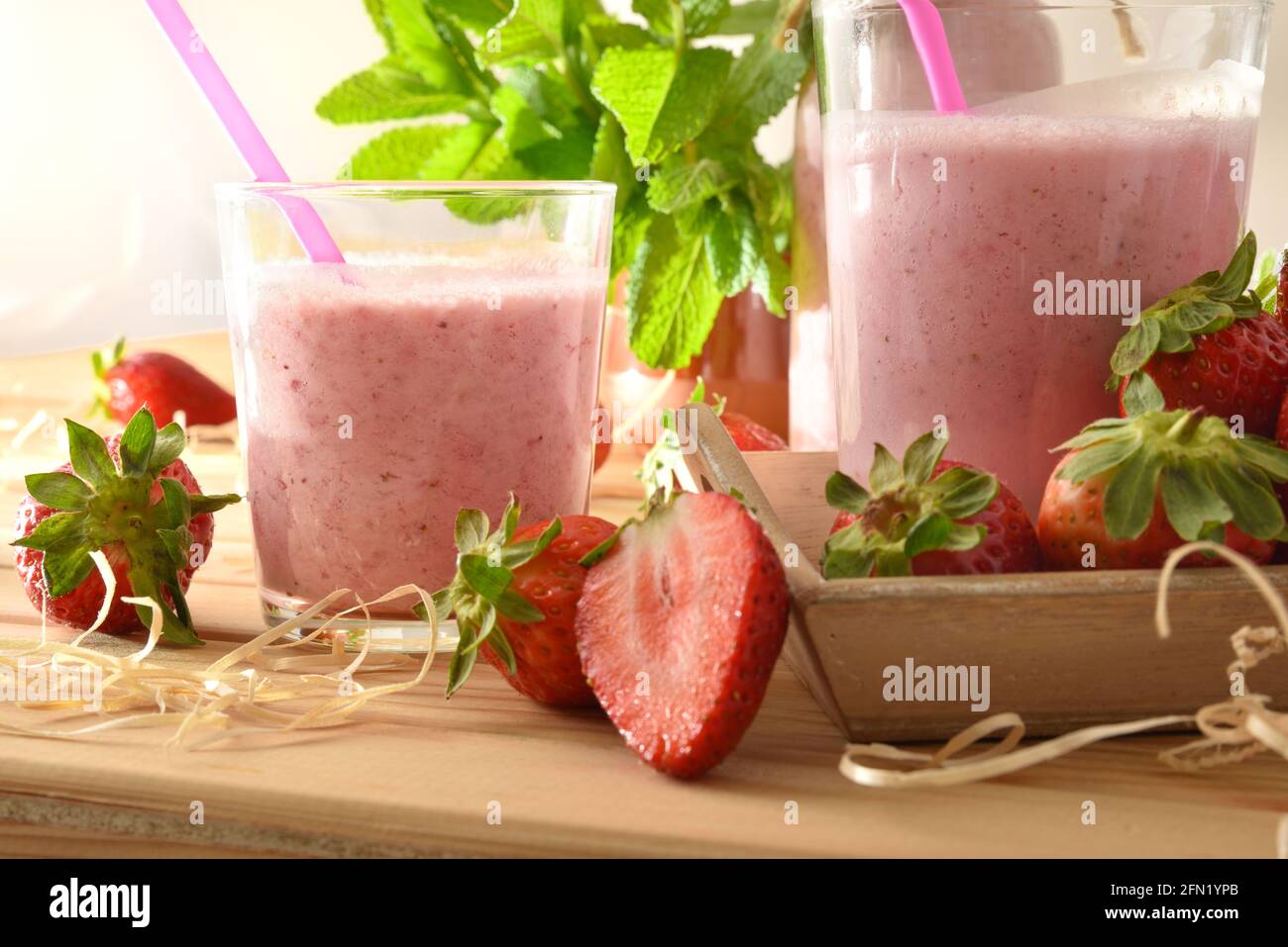 Erdbeermilchshake in Glasbehältern auf Holztisch mit Tablett voller Erdbeeren in der Natur aus nächster Nähe. Vorderansicht. Stockfoto