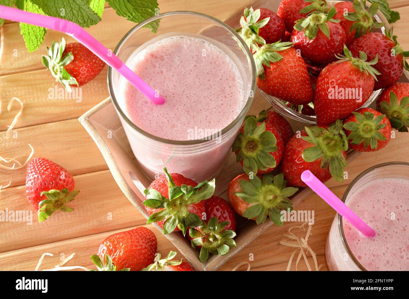 Erdbeer-Smoothie mit Milch in Glasbehältern auf Holztisch mit Tablett voller Erdbeeren in der Natur. Ansicht von oben. Stockfoto