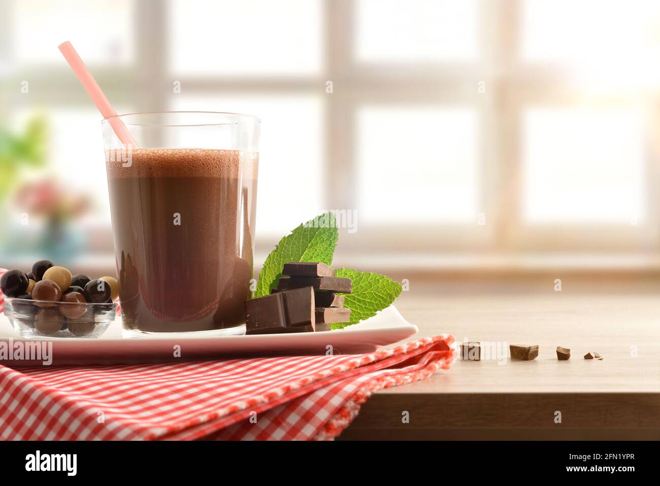 Glas mit Milchschokolade schütteln auf Servierteller mit Schüssel Voller Schokoladenkugeln und Portionen auf rot und weiß Karierte Tischdecke auf einem Tisch mit l Stockfoto