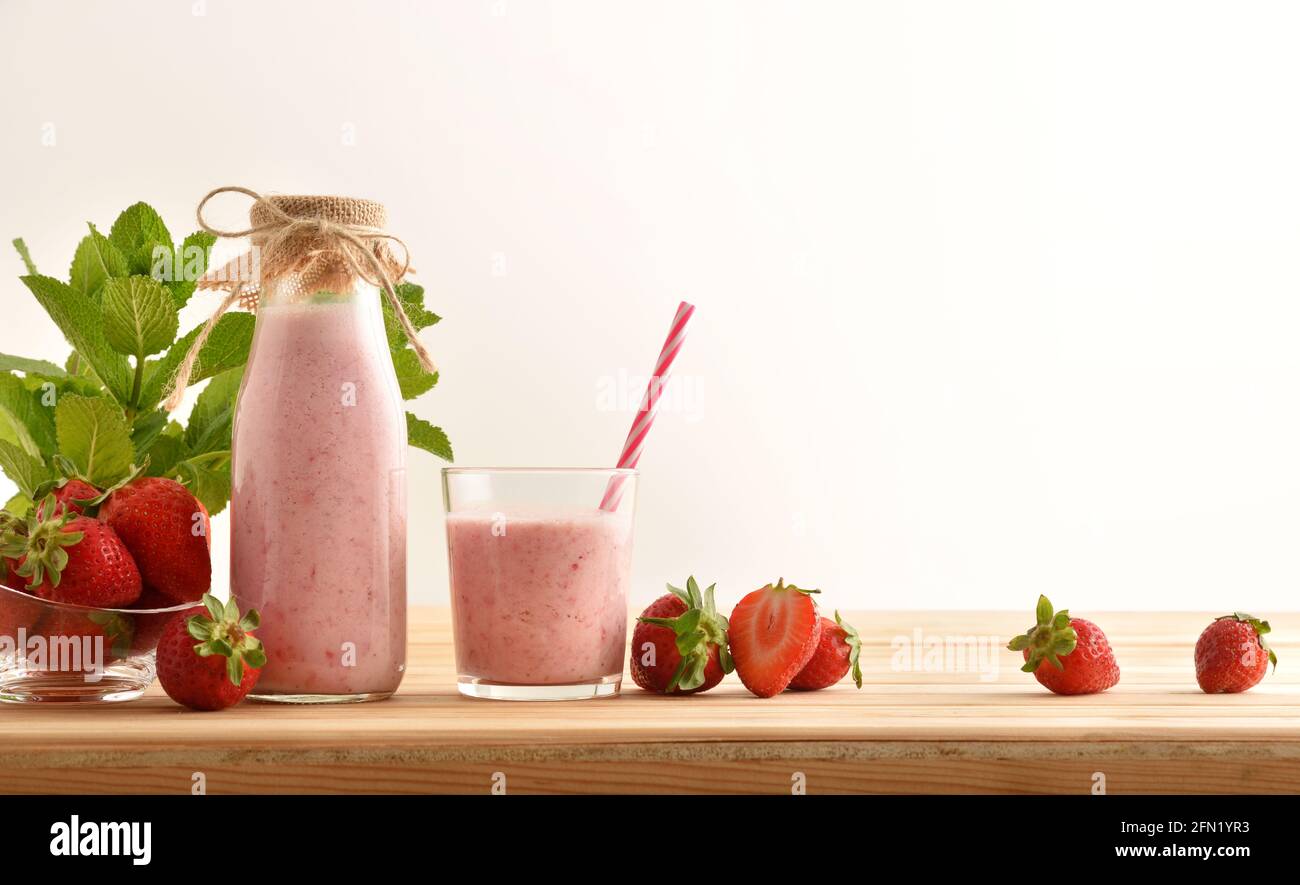 Flasche und Glas voller Erdbeer-Smoothie auf Holztisch voller Früchte isoliert Hintergrund. Vorderansicht. Stockfoto