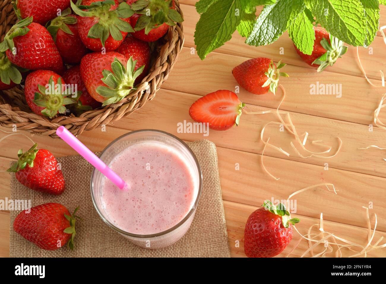 Erdbeershake mit Milch im Glas auf Holztisch mit Korb voller Erdbeeren in der Natur. Draufsicht. Stockfoto