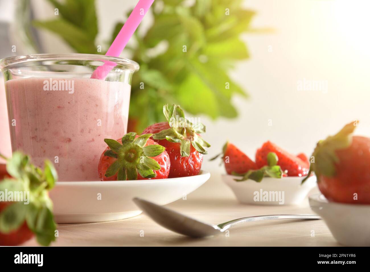 Erdbeer-Joghurt-Smoothie auf Holztisch mit Schalen voller Erdbeeren. Vorderansicht. Stockfoto
