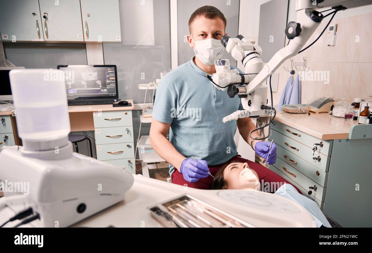 Männlicher Zahnarzt mit sterilen Handschuhen, der Kieferorthopädie und Spiegel hält, während die Patientin auf dem Zahnstuhl liegt. Konzept der Zahnmedizin, Stomatologie und Zahnpflege. Stockfoto