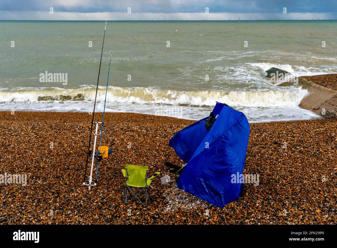Ein Fischer versucht, sein Zelt an EINEM windigen Tag am Hove Beach, Hove, East Sussex, Großbritannien, einzurichten. Stockfoto