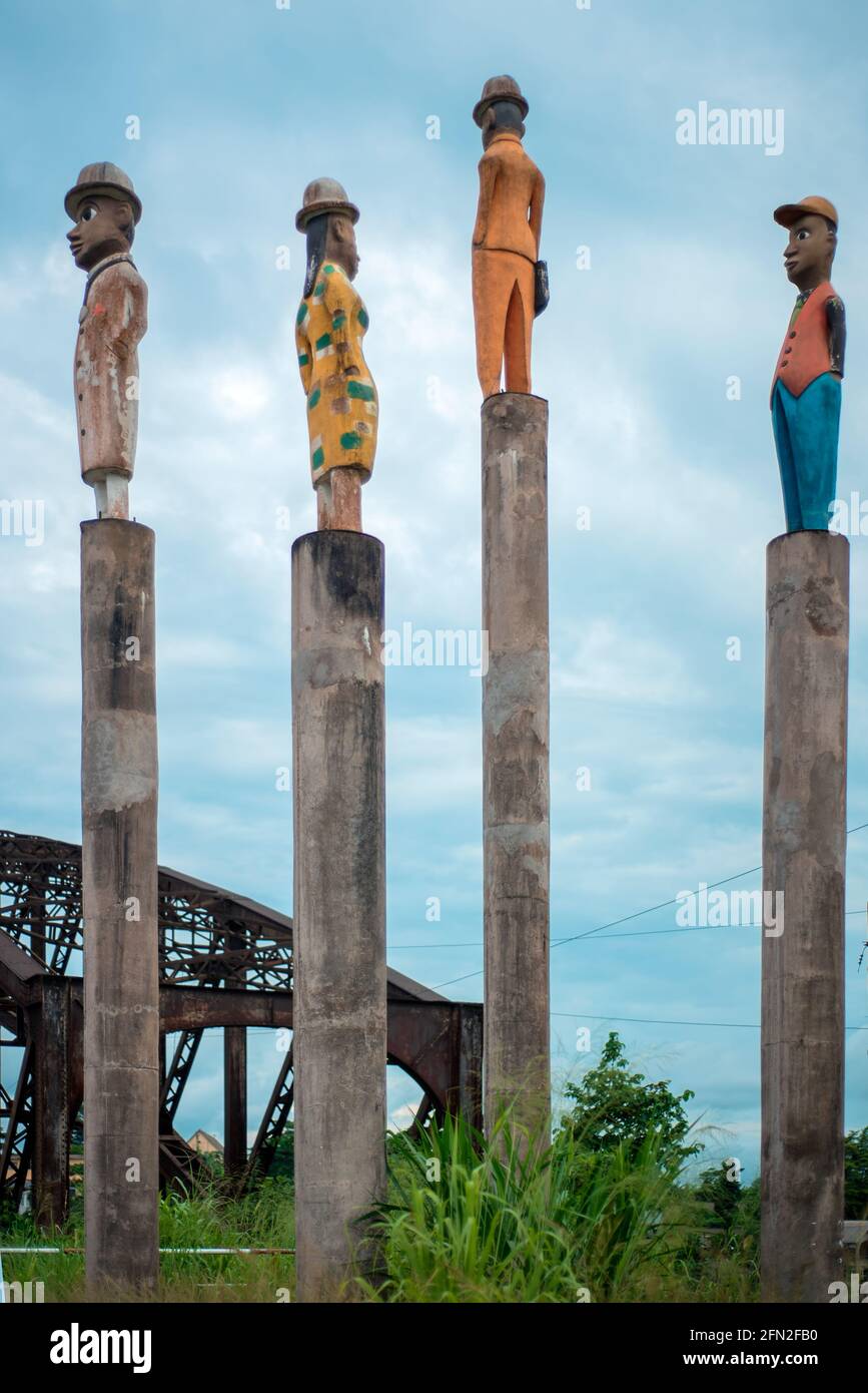 Vier Holzstatuen mit Hüten auf Stöcken im alten Sanaga River Bridge Stockfoto