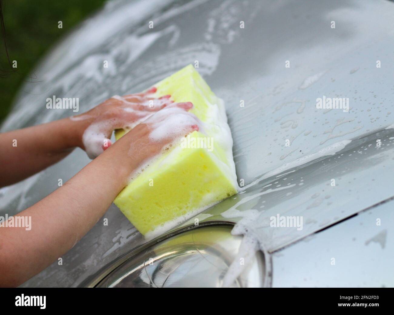 Die Hand eines kleinen Kindes mit einem Schaumschwamm wäscht das Haube des  Autos Stockfotografie - Alamy