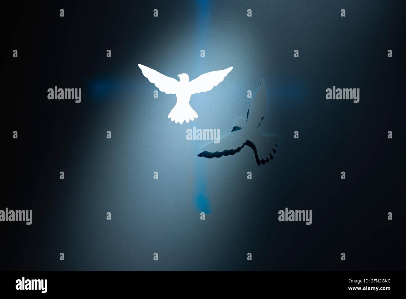 Zwei Tauben Silhouetten über einem blauen Kreuz auf dunklem Hintergrund. Religiöses Thema. Stockfoto