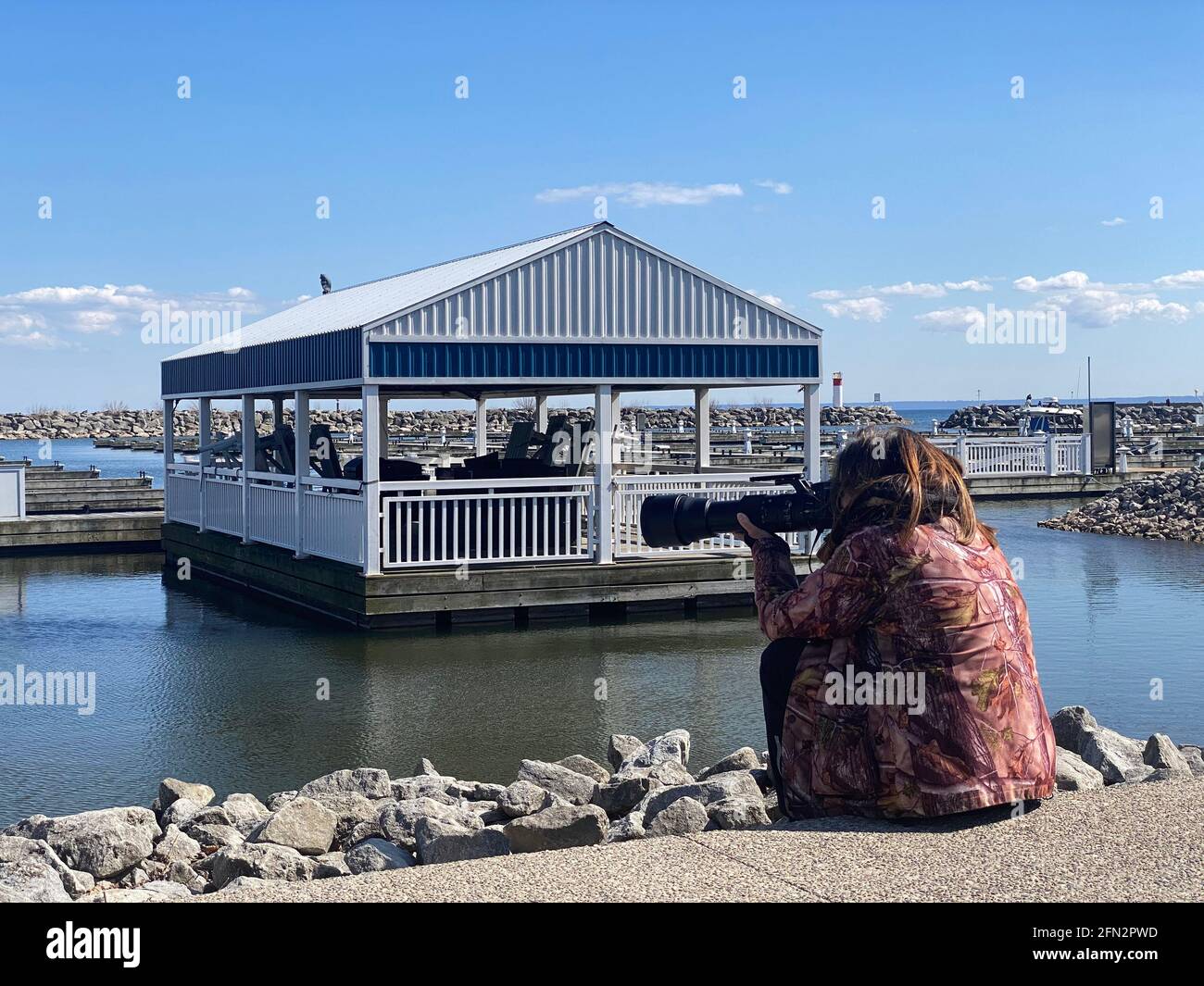 DER FOTOGRAF SITZT AM PIER UND FOTOGRAFIERT VÖGEL MIT LANGER LINSE WÄHREND DER COVID-19-PANDEMIE. Stockfoto