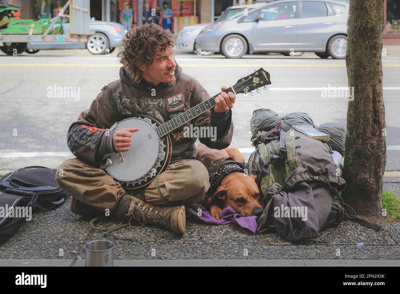 Vancouver, Kanada - 25 2014. April: Stadtporträt eines Obdachlosen-Straßenmusikers, der mit seinem Hund auf dem Commercial Drive in East Vancouver das Banjo spielt Stockfoto