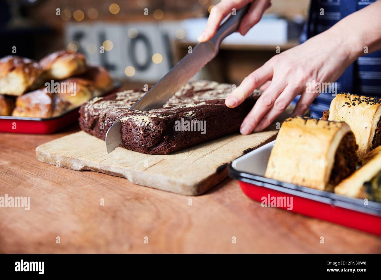 Verkaufsassistent In Bäckerei Schneiden Frisch Gebackene Brownies Auf Zähler Stockfoto
