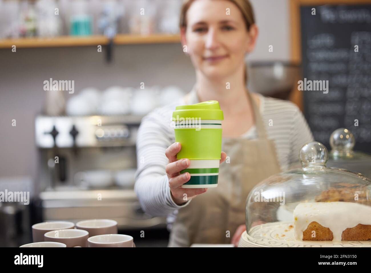 Weibliche Mitarbeiterin im Café serviert Kaffee in einer nachhaltigen wiederverwendbaren Tasse Stockfoto