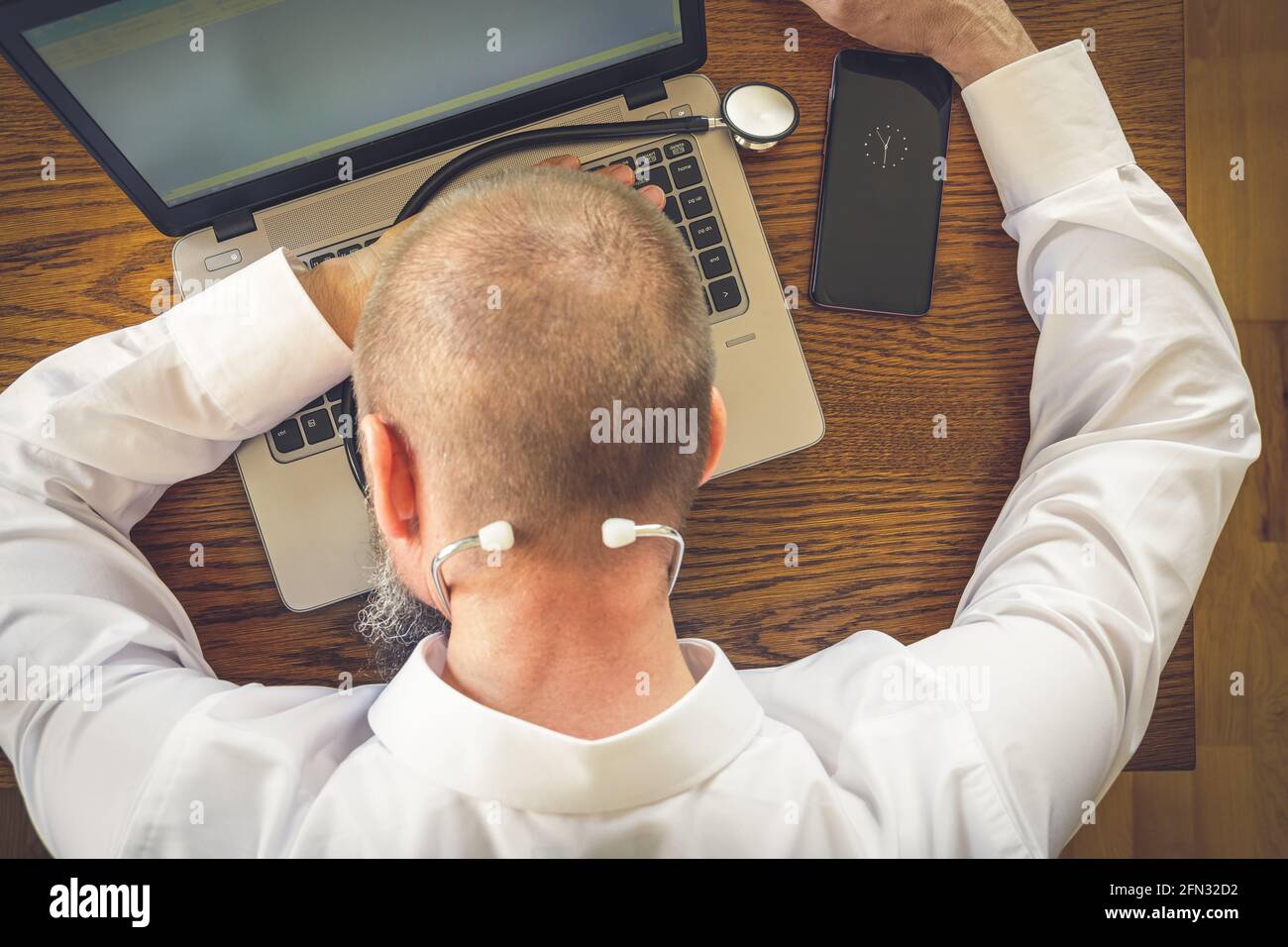 Telemedizin, erschöpfter Arzt nach einem Arbeitstag mit einem Nickerchen auf seinem Laptop Stockfoto