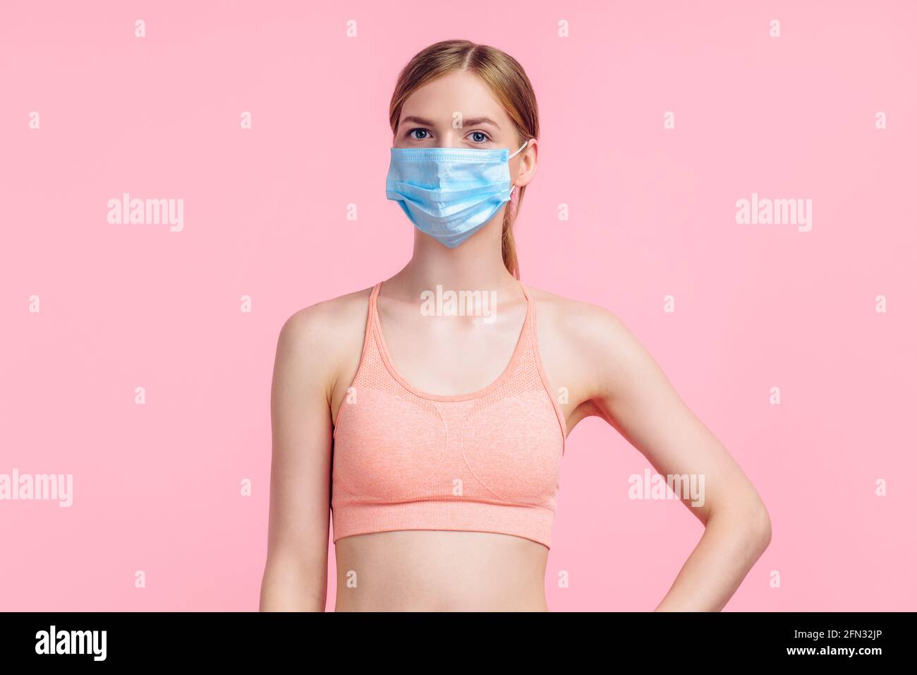 Schöne junge Fitness-Frau trägt Schutzmaske, um Corona-Virus zu verhindern, Sportlerin mit perfektem Körper trägt Sportbekleidung für Workouts, auf isoliert Stockfoto