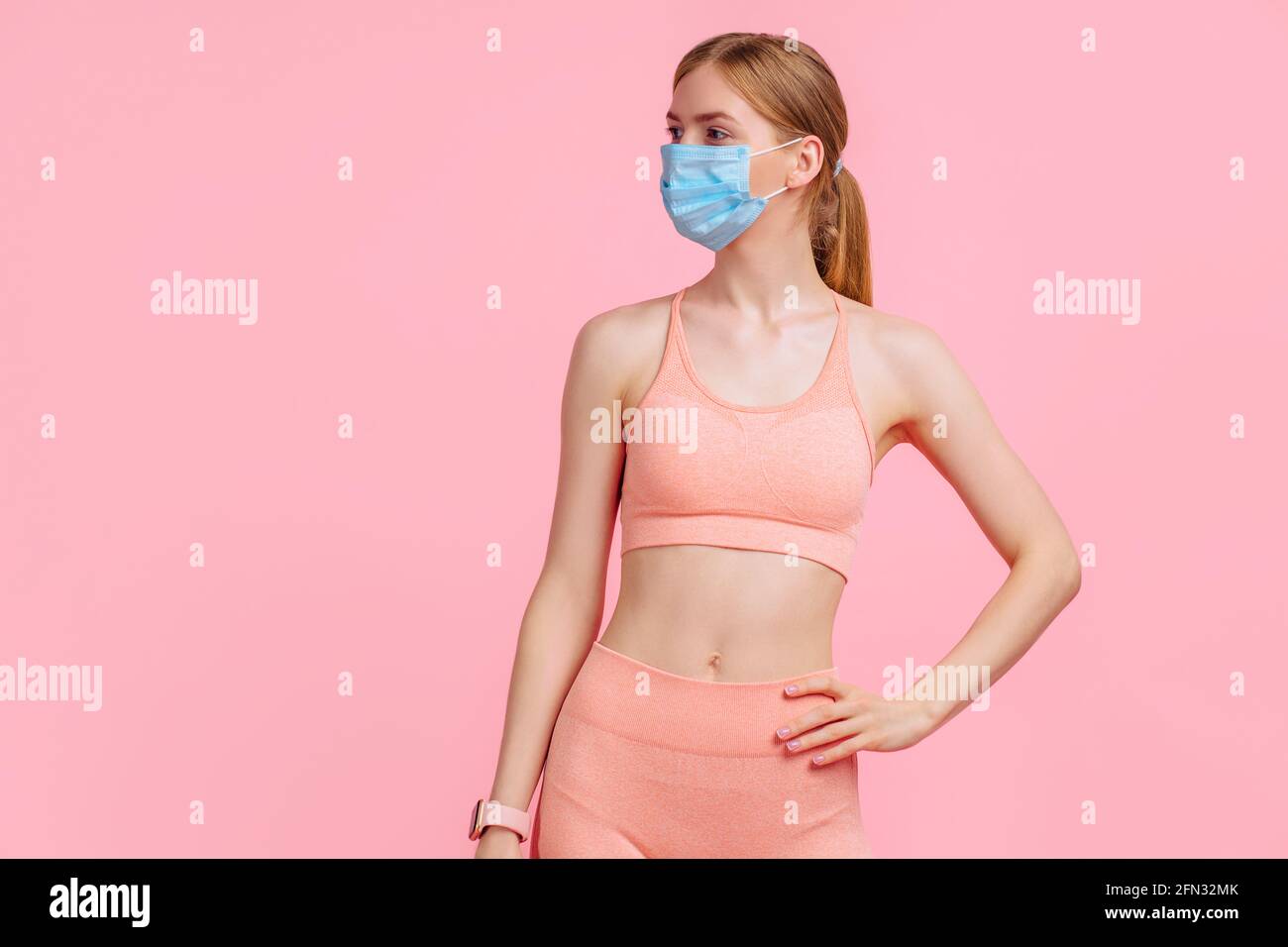 Schöne junge Fitness-Frau trägt Schutzmaske, um Corona-Virus zu verhindern, Sportlerin mit perfektem Körper trägt Sportbekleidung für Workouts, auf isoliert Stockfoto