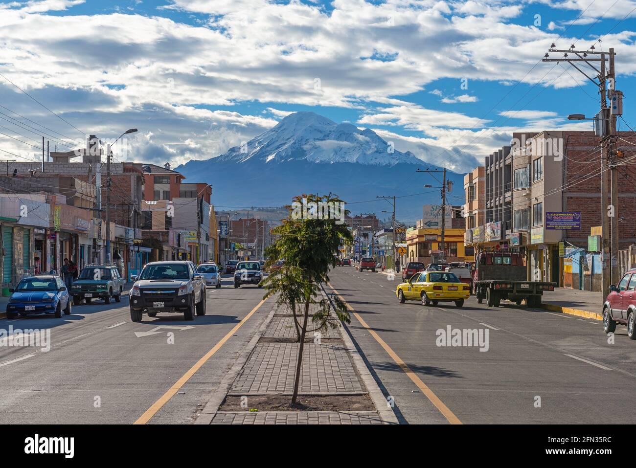 Hauptstraße von Riobamba Stadt mit Autos und Fassaden in Linie mit dem Chimborazo Vulkan. Konzentrieren Sie sich auf Gebäude und Vulkan. Stockfoto