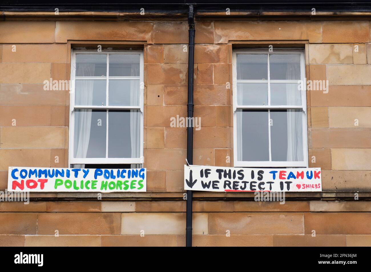 Glasgow, Schottland, Großbritannien. Mai 2021. Gegen 5.30 Uhr ließ die Polizei zwei Männer aus einem Haftfahrzeug des Innenministeriums frei. In Begleitung des Anwalts Aamer Anwar gingen die Männer zu einer nahe gelegenen Moschee, umgeben von Hunderten von Polizisten und Unterstützern, die zuvor das Fahrzeug umzingelt hatten und auf der Straße saßen. Foto: Protestschilder hingen vor den flachen Mietskaserfenstern. Kredit: Iain Masterton/Alamy Live Nachrichten Stockfoto
