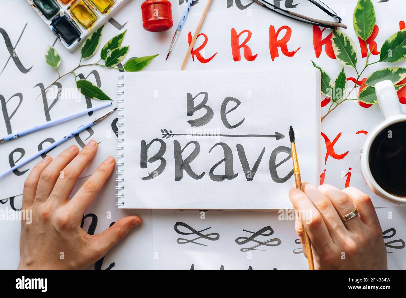 Overhead-Ansicht auf männlichen Mann Hände Kalligraphie Blätter, Schreibfedern, Papier, Tinte rote Stifte.Handwerk, Hobby. Lettering Workshop.Flat Lay Motivationsschreiben Worte Quo Stockfoto