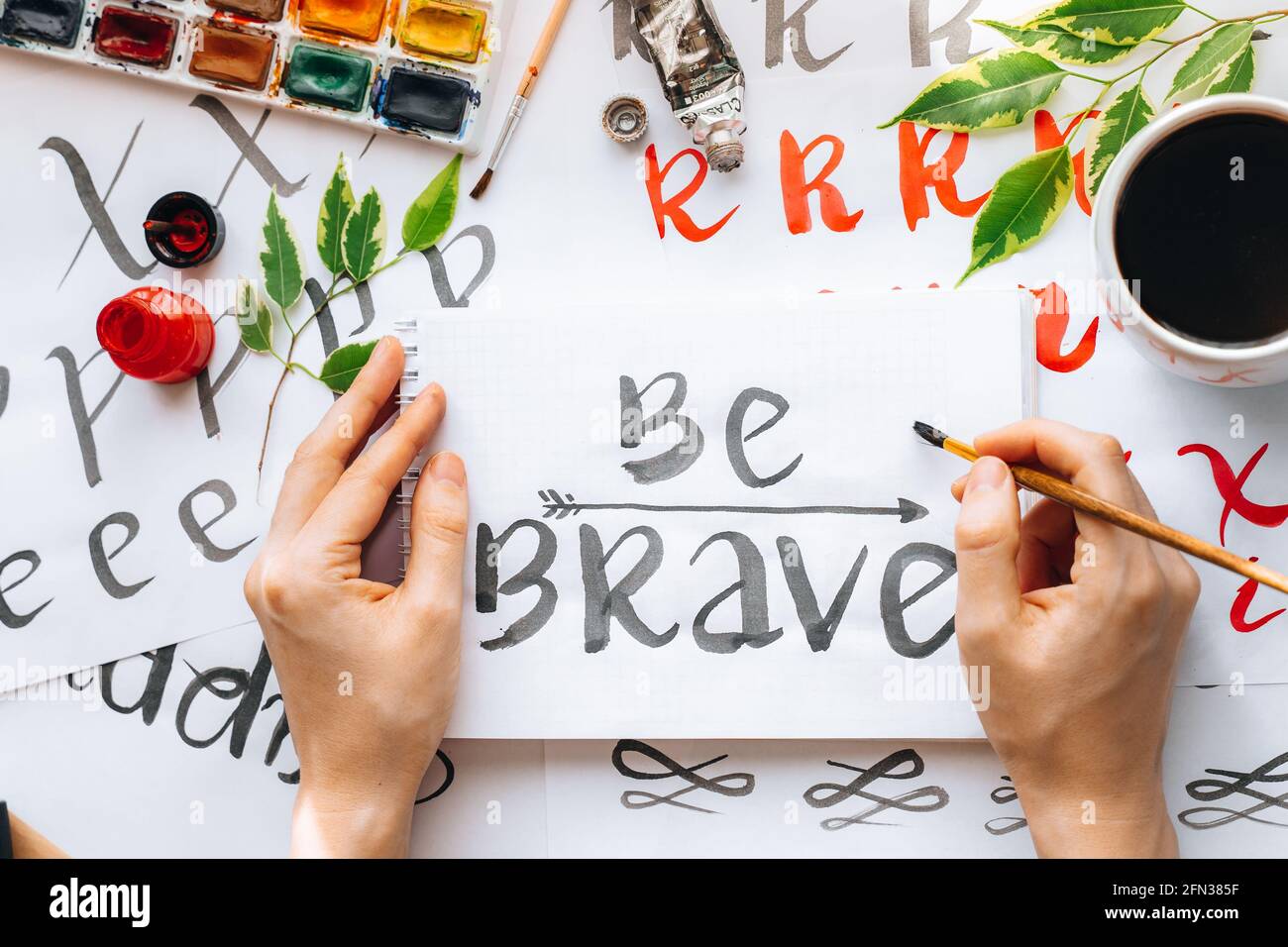 Overhead-Ansicht auf männlichen Mann Hände Kalligraphie Blätter, Schreibfedern, Papier, Tinte rote Stifte.Handwerk, Hobby. Lettering Workshop.Flat Lay Motivationsschreiben Worte Quo Stockfoto