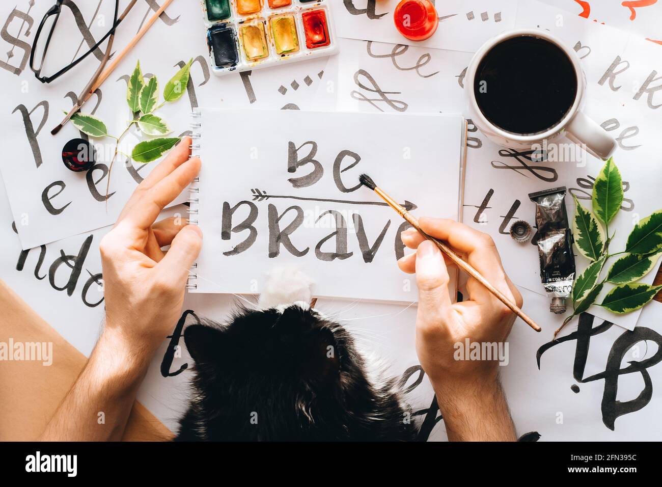 Ansicht von oben Mann und Katze schreiben auf Papierbogen Leinwand Kalligraphie Wort MUTIG zeichnen mit schwarzer roter Tinte Pinsel.Creative Künstler freiberuflich in zu Hause studi Stockfoto