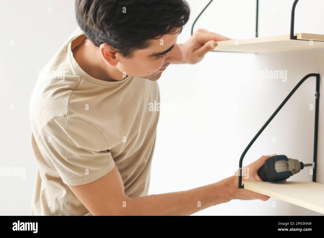 Junger Mann installiert moderne Regale im Zimmer Stockfoto