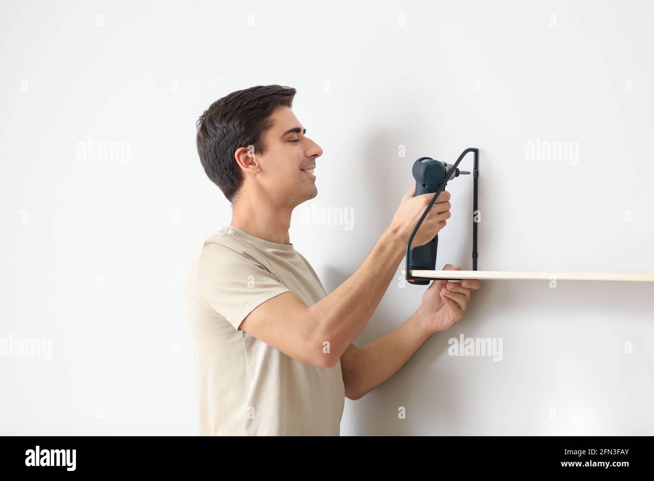 Junger Mann installiert modernes Regal im Zimmer Stockfoto
