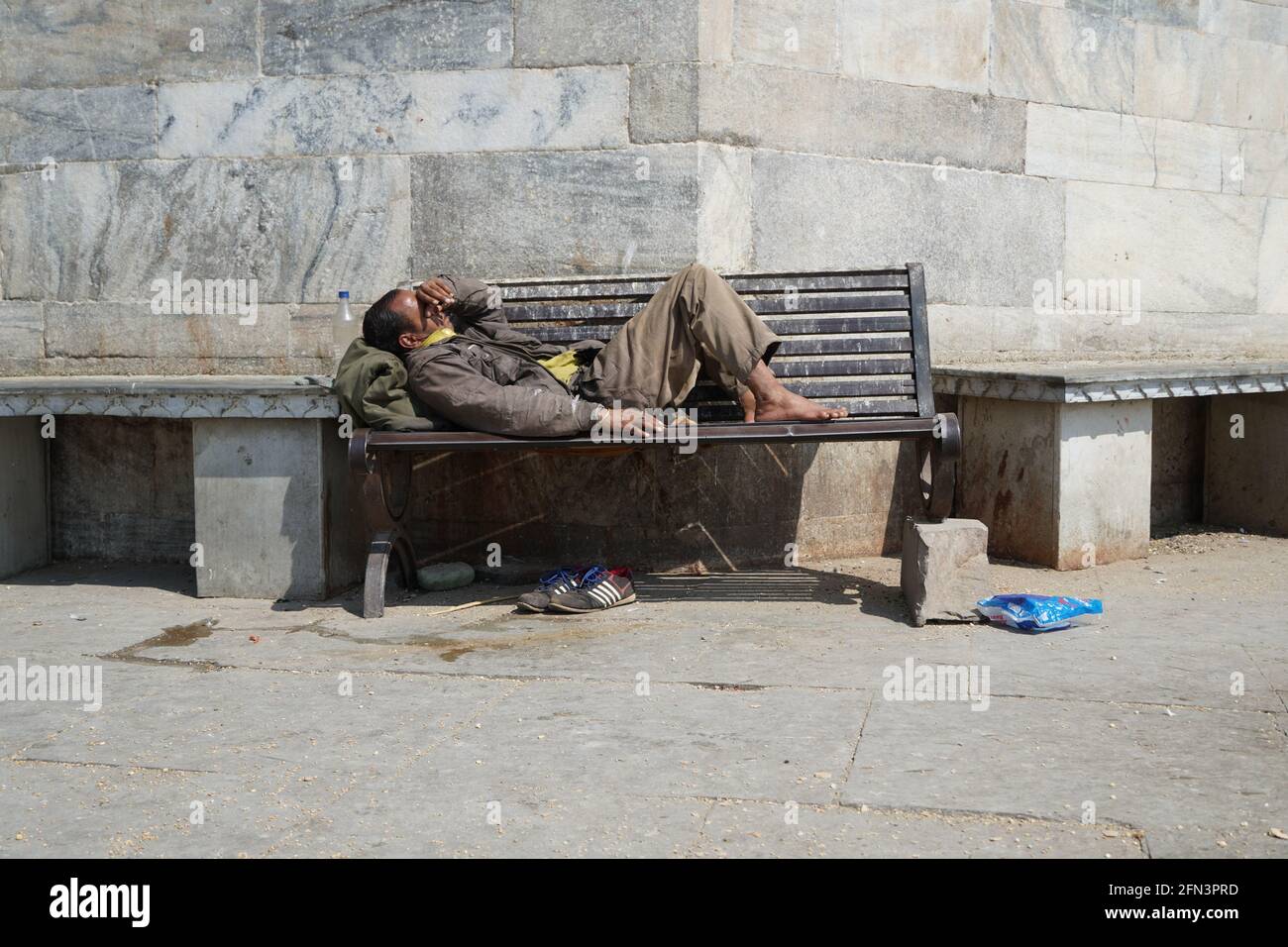Armer obdachloser Bettler oder Flüchtling, der tagsüber auf einer schmutzigen Holzbank in einer Einbahnstraße in der Stadt schläft. Sozialdokumentarisches Konzept. Schuh Stockfoto