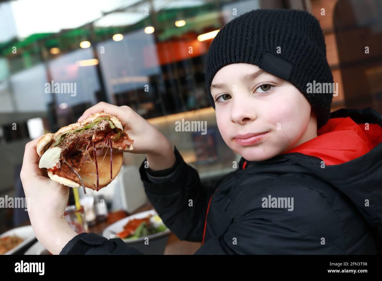Das Kind hat im Frühling Burger auf der Restaurantterrasse Stockfoto