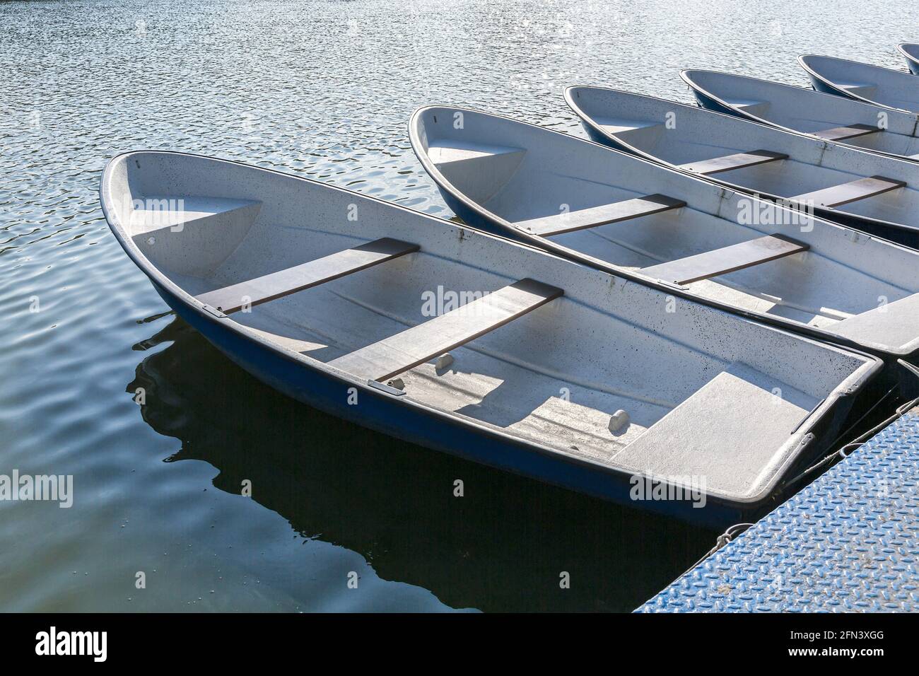 Blaue Fiberglas-Boote sind am Pier am Flussufer vertäut. Ruderboote zum Verleih. Stockfoto