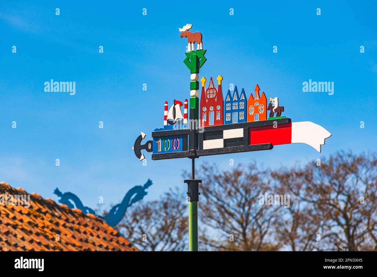 Schöner, farbenfroher Wetterhahn, der in der Kurischen Nehrung im Fischerdorf Nida, Litauen, Europa, mit blauem Himmel und einem Dach mit Pferdeköpfen winkt Stockfoto