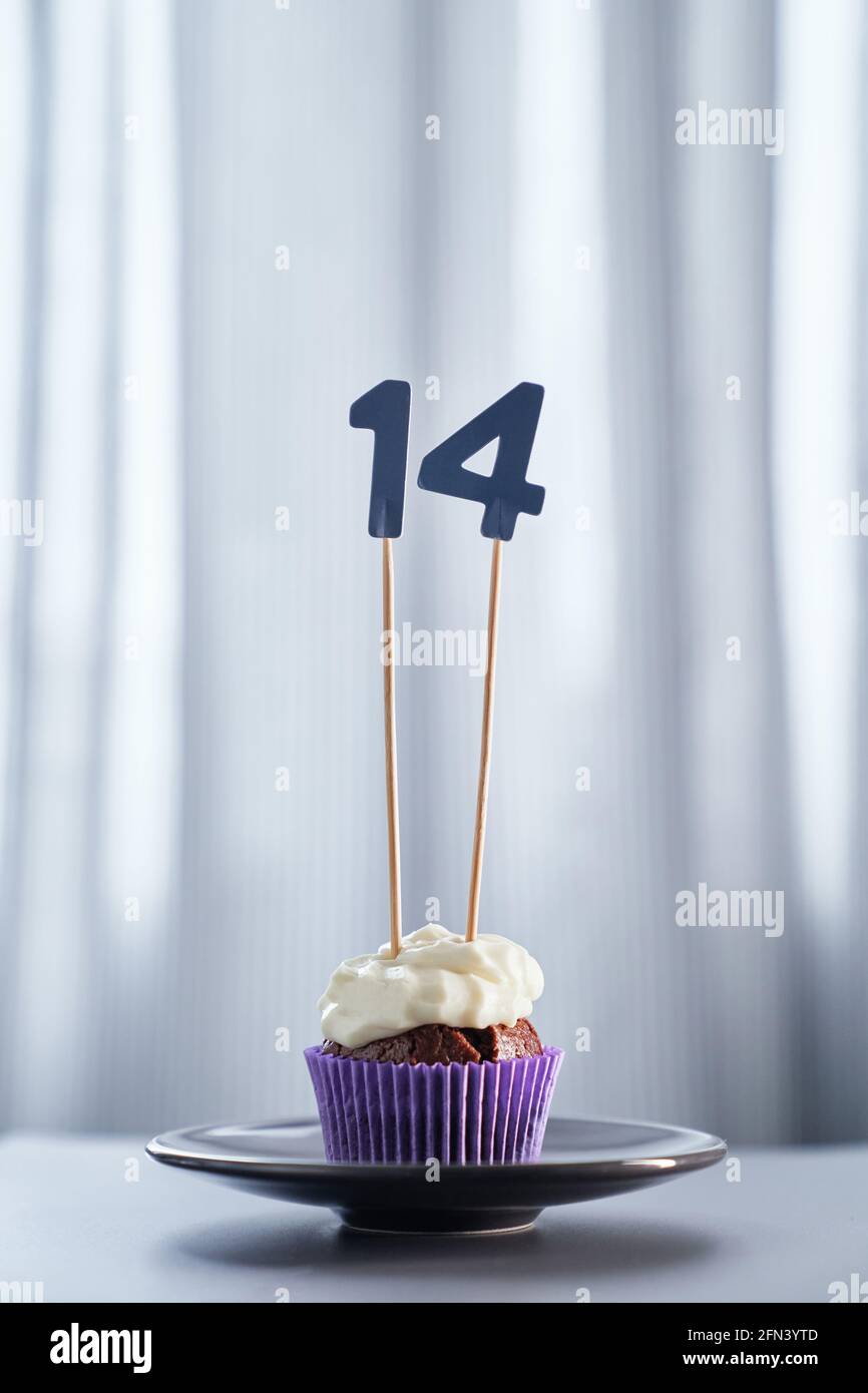 Geburtstags- oder Jubiläumskuchen-Konzept. Hausgemachte Schokolade Geburtstag Cupcake mit cremigen Belag und Nummer 14 vierzehn auf schwarzem Teller und hellen Hintergrund. Hochwertiges vertikales Bild Stockfoto