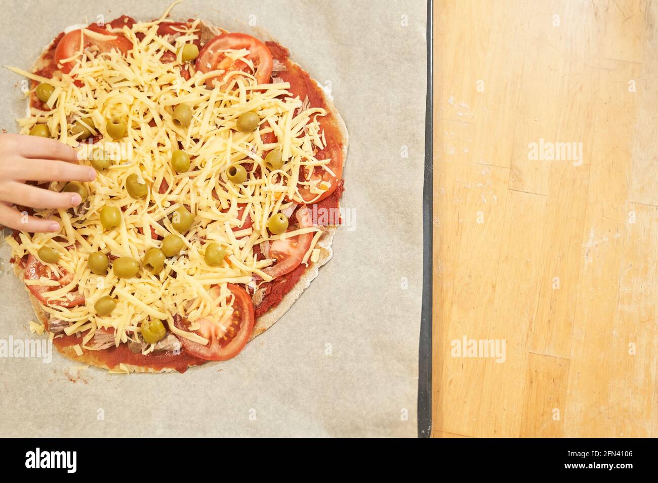 Childs Hand mit Pizza auf Backpapier zum Backen vorbereitet. Gesunde glutenfreie Pizza. Glutenfreier Kochkurs. Foto mit Kopierbereich. Stockfoto