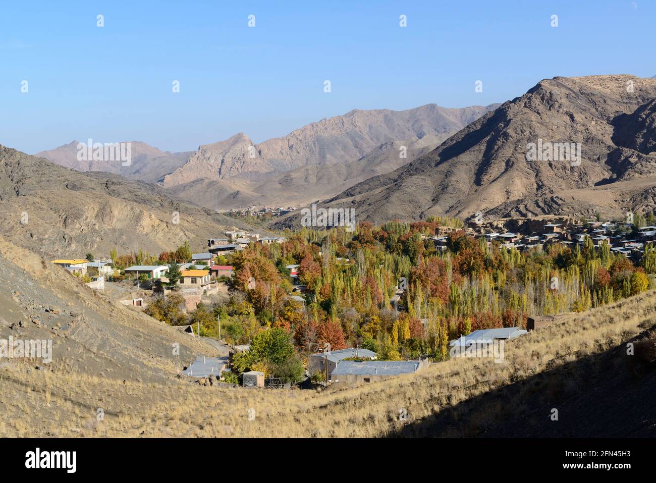 Ein Dorf mit Bäumen in Herbstfarben in einem Tal im Natanz County, Provinz Isfahan, Iran. Stockfoto