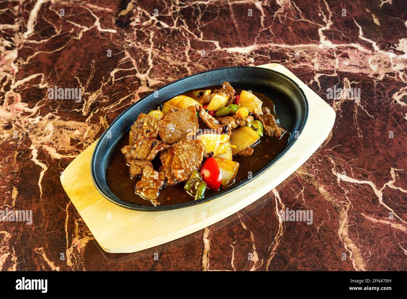Asiatisches Rindfleischgericht mit herzhafter Sauce und etwas Gemüse, das auf einem heißen Teller unter einer marmorierten Oberfläche serviert wird. Stockfoto