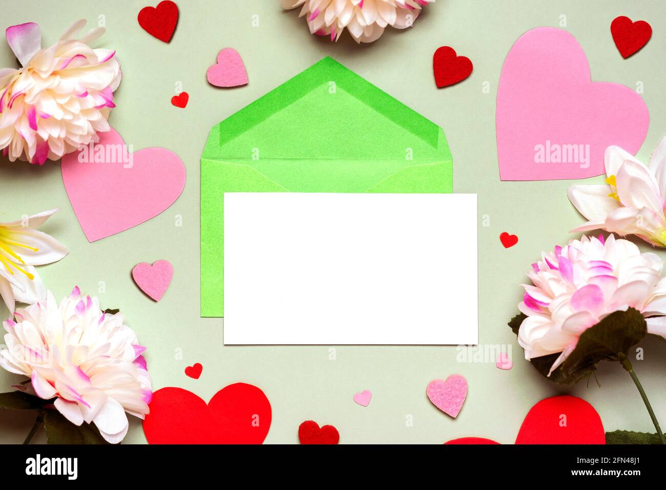Grußkarte. Grüner Umschlag und weißes Papier mit Kopierraum, Blumen und Herzen auf grünem Hintergrund. Herzlichen Glückwunsch zum Muttertag, Geburtstag und Stockfoto