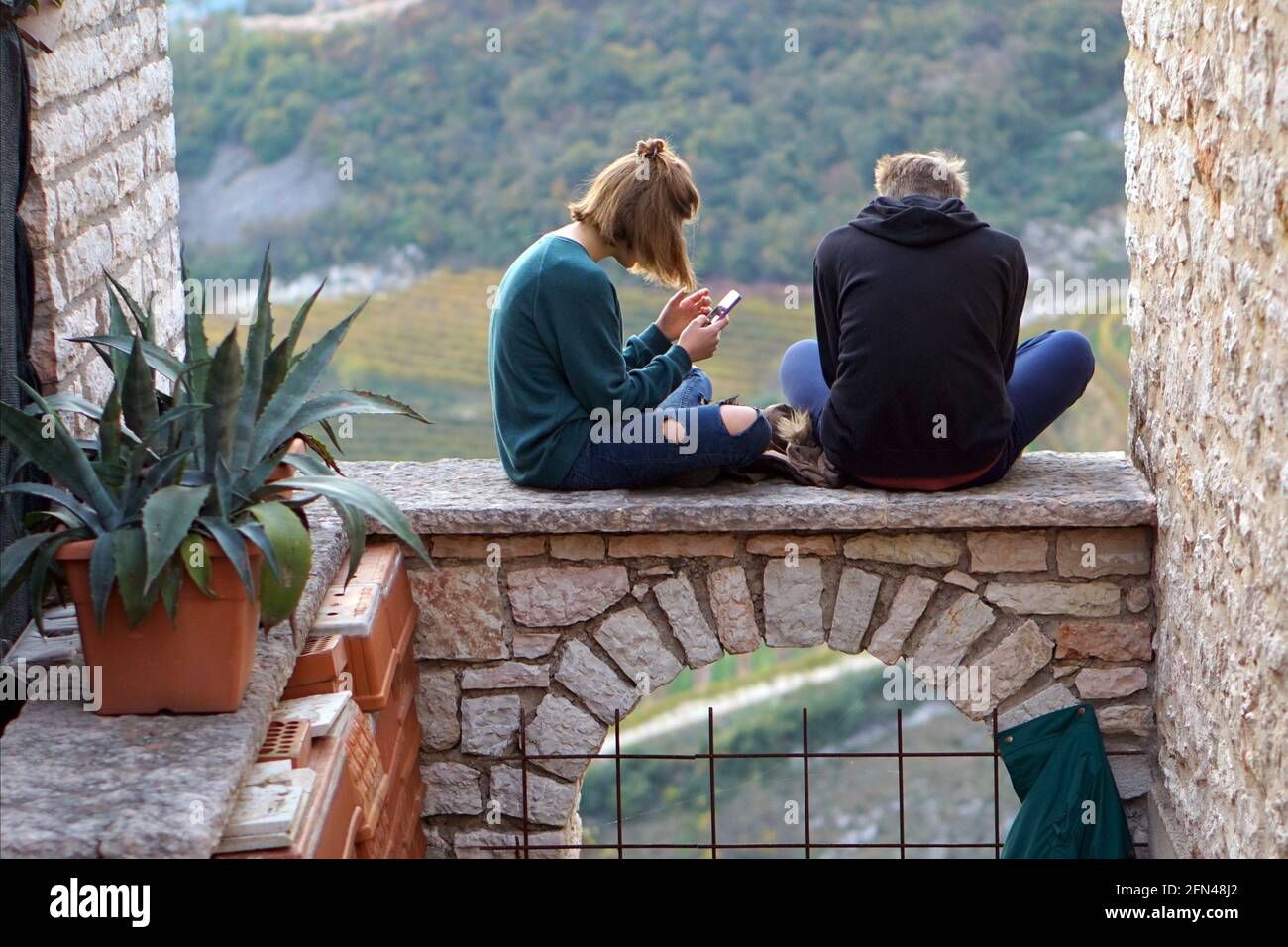 Teenager saßen auf einem Bogen. Neue Technologien und alte Architekturen. Jugendliche nutzen ihre Handys im Freien. Stockfoto